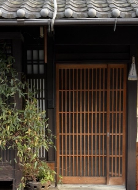 京都の路地に佇む京町家。木の格子戸と瓦屋根、軒下の植え込みに京都の暮らしの気配が漂う