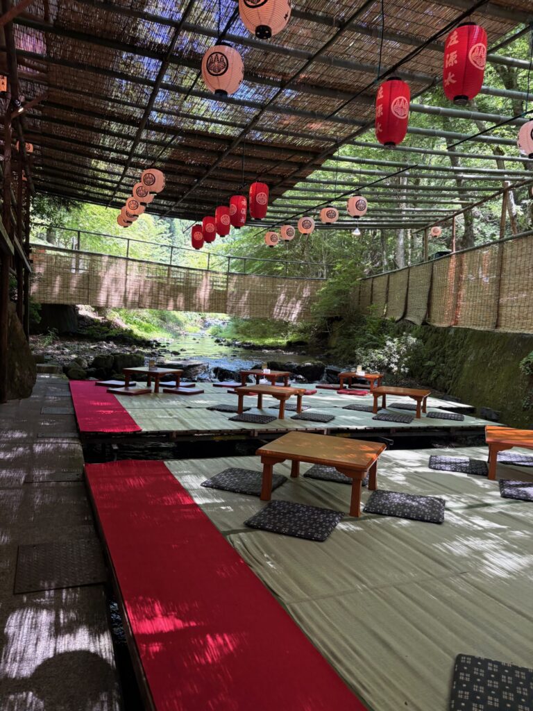 開店直後の誰もいない左源太の川床。赤い提灯と座卓が並ぶ川の上の座敷と青もみじ