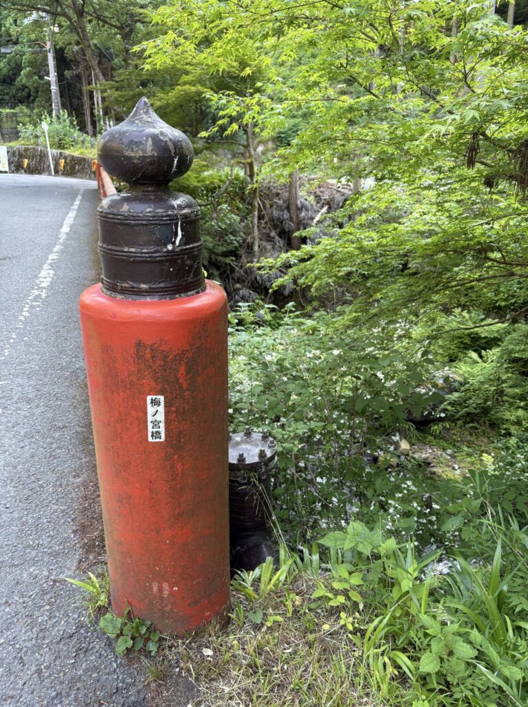 貴船川にかかる「梅ノ宮橋」の赤い親柱と、川沿いの新緑