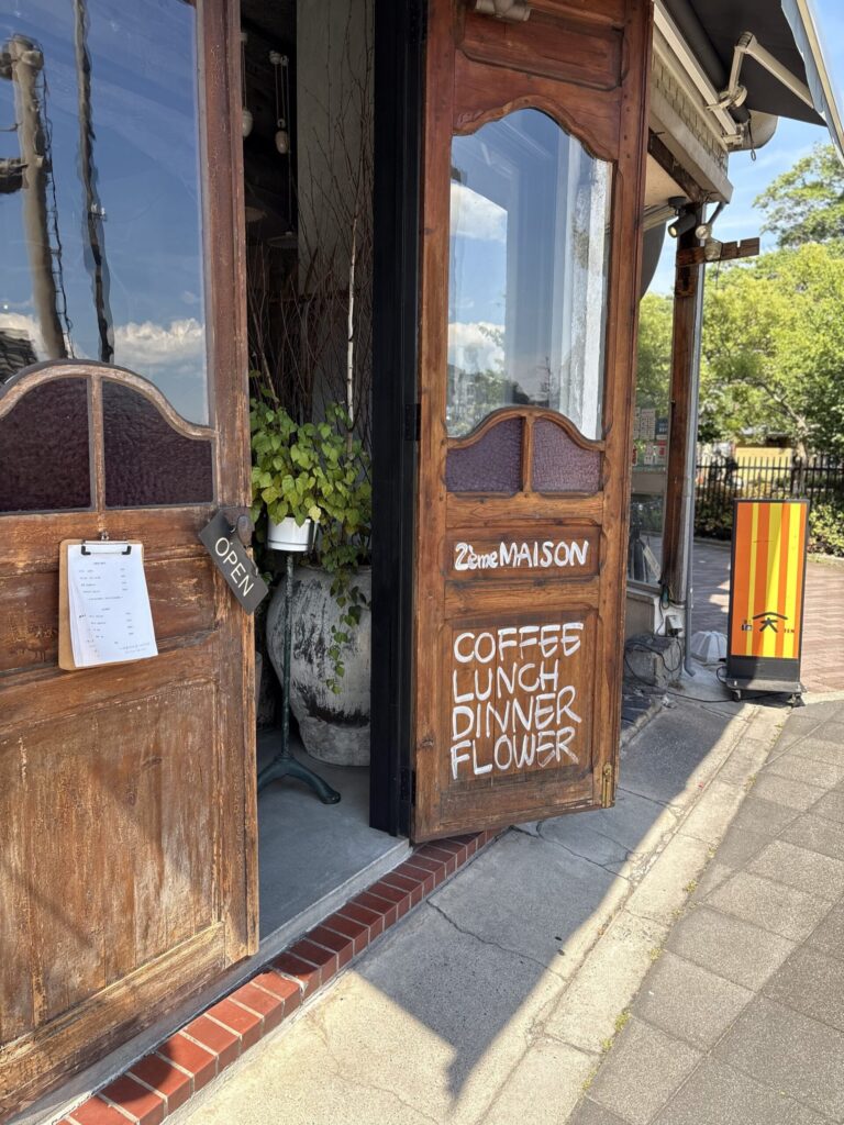 ドゥージィエムメゾンの外観。木の扉に「COFFEE LUNCH DINNER FLOWER」の白い手書き文字