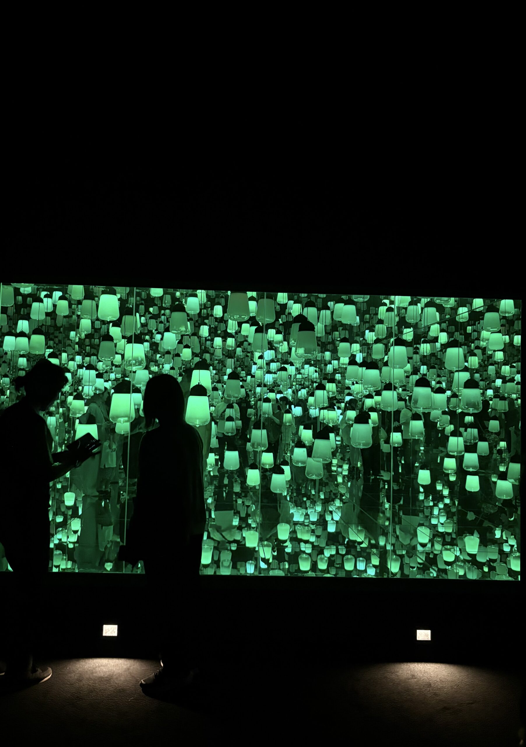 暗い展示室で、鏡に映り込む緑色に光る無数のランプ