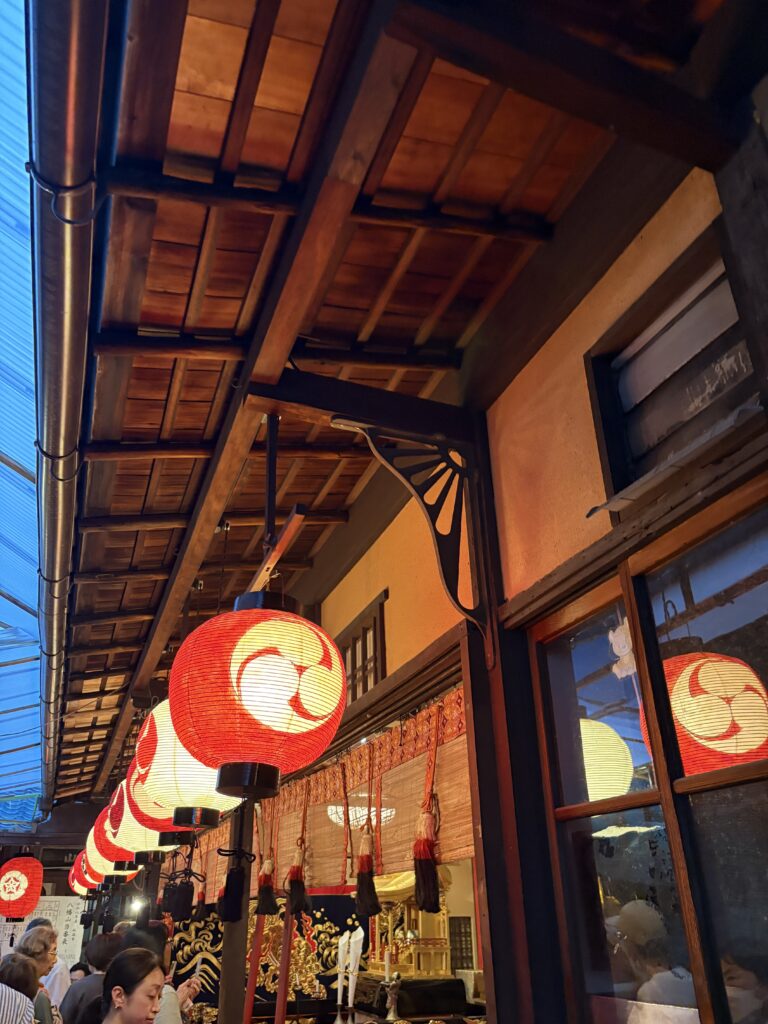 祇園祭 後祭・八幡山の会所。軒下に並ぶ三つ巴紋の赤い提灯と、奥に見える金色の社殿
