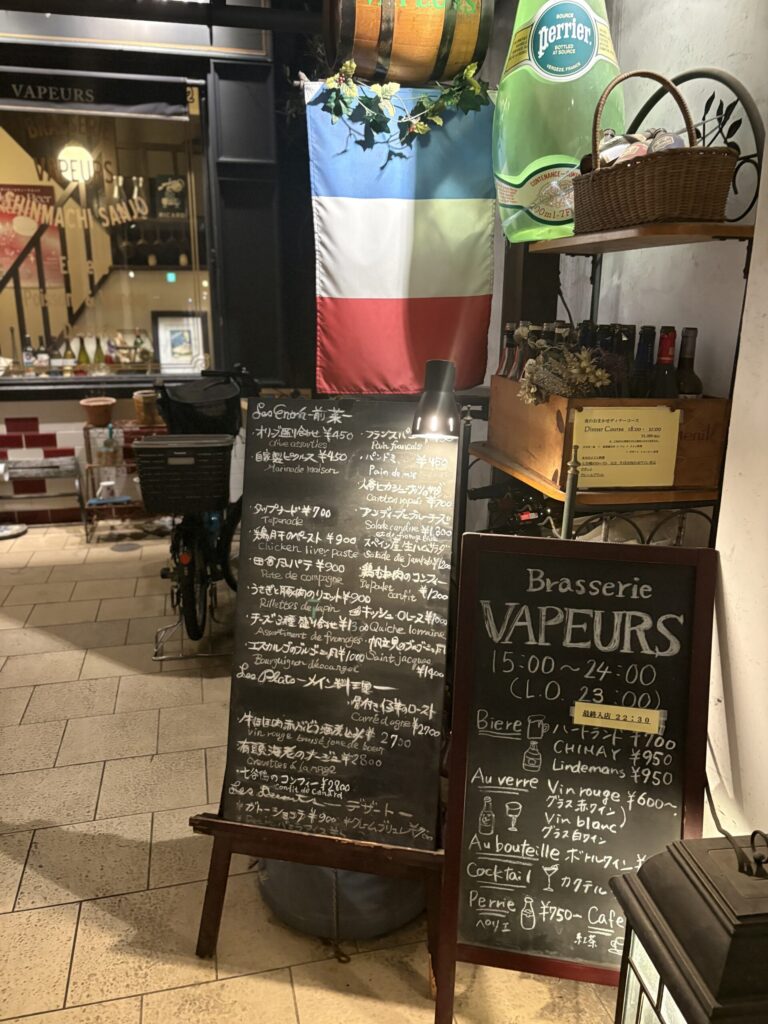 Brasserie VAPEURS の入口。黒板メニューとフランス国旗、大きなペリエのボトルが置かれている