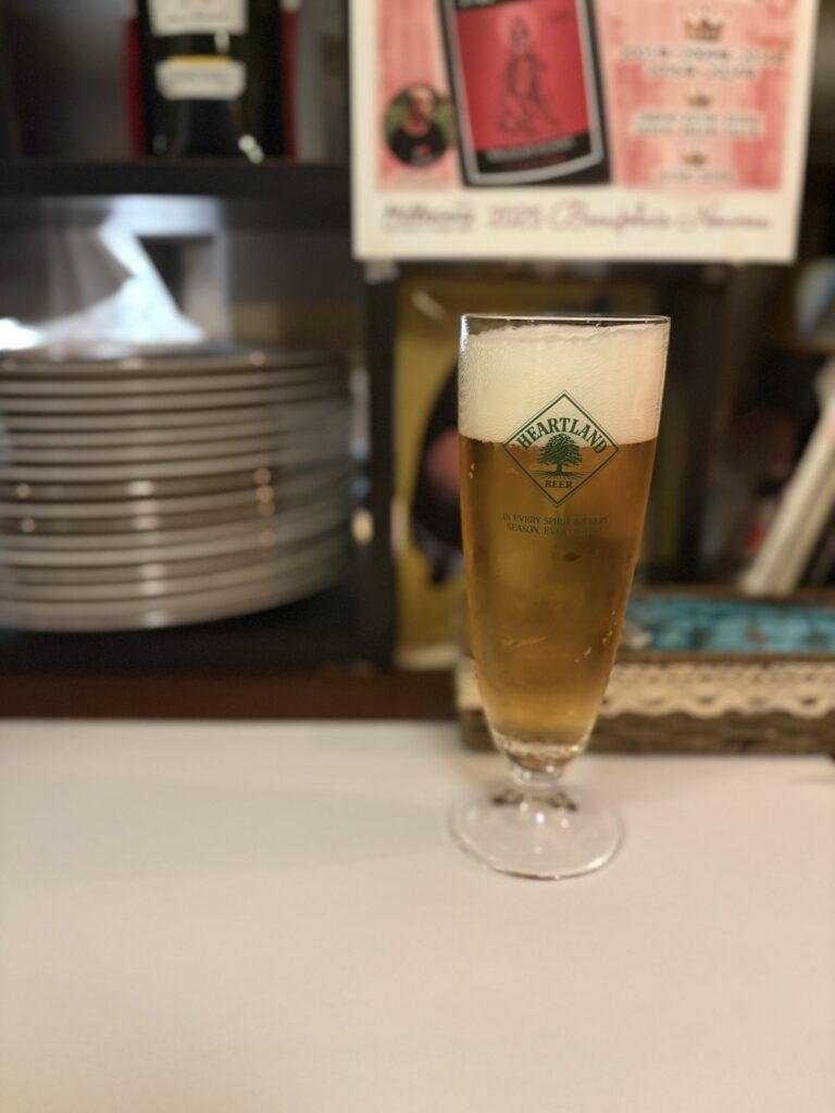 ハートランドビールの脚付きグラス。奥にカウンターに重ねられた皿