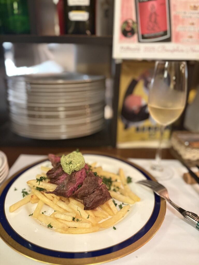 フライドポテトを敷いた牛肉の、ステーキ。上に緑のハーブバターがのっている