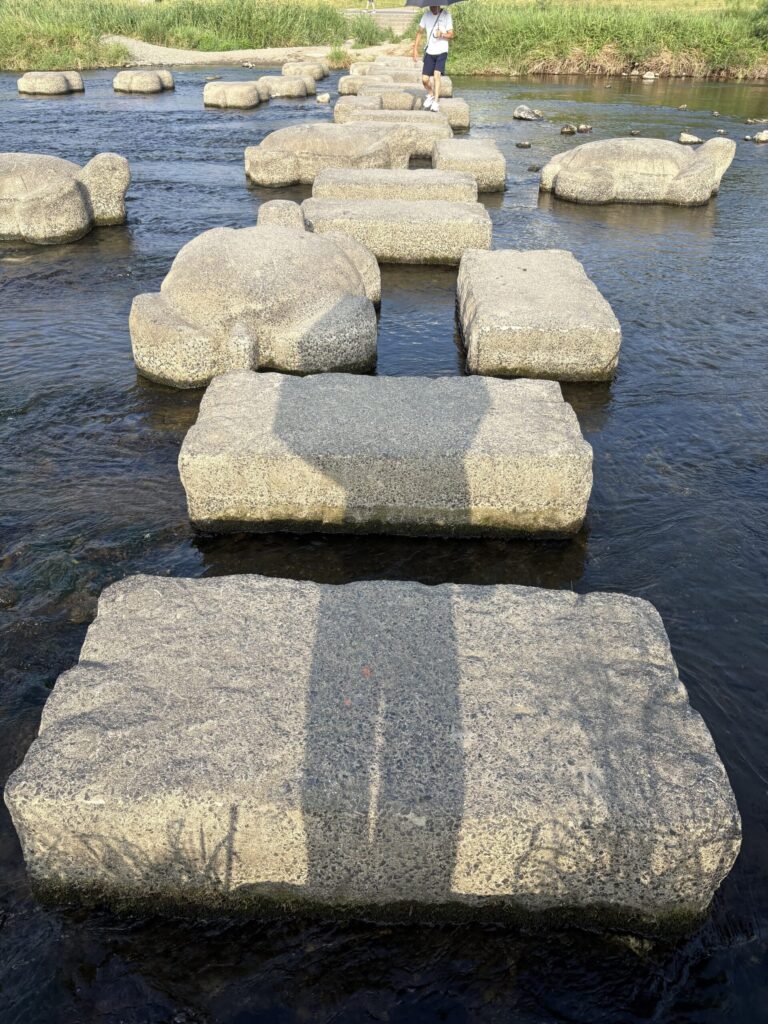 鴨川デルタの飛び石。亀の形をした石が水の中に並び、奥を日傘の人が渡っていく