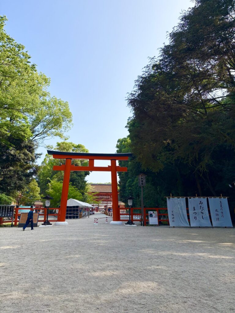 みたらし祭の朝の下鴨神社。朱の鳥居の脇に「真夏の京の風物詩 みたらしまつり」の幕が下がる