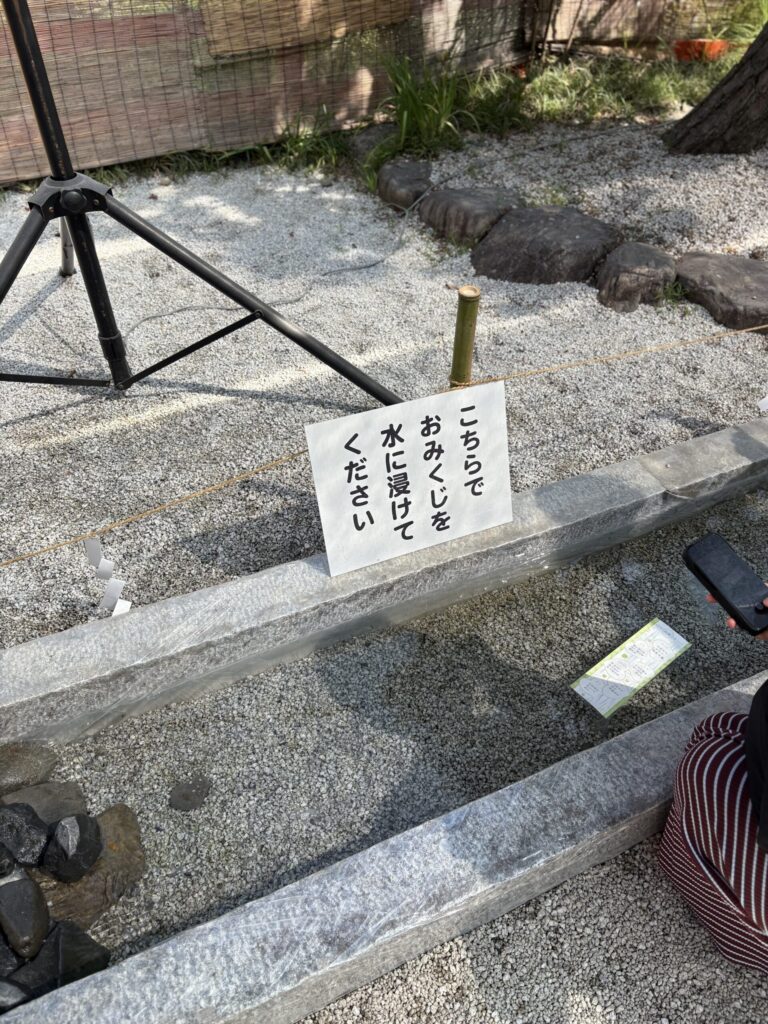 「こちらでおみくじを水に浸けてください」の立て札と、水の流れる石の水路