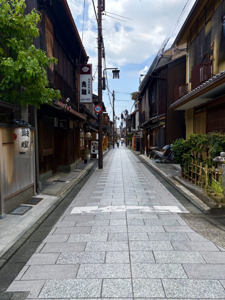 京町家が軒を連ねる石畳の路地。奥に和傘をさして歩く人の後ろ姿