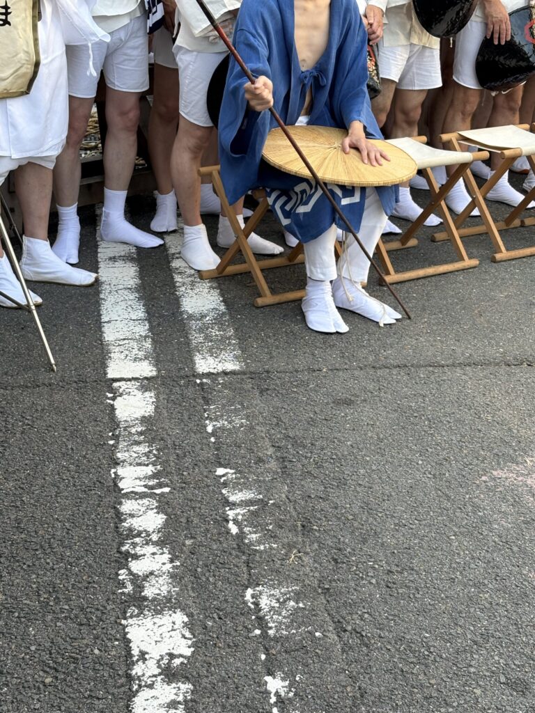 祇園祭 後祭・巡行の朝。白足袋の足が並ぶなか、菅笠を手に床几に腰かける人