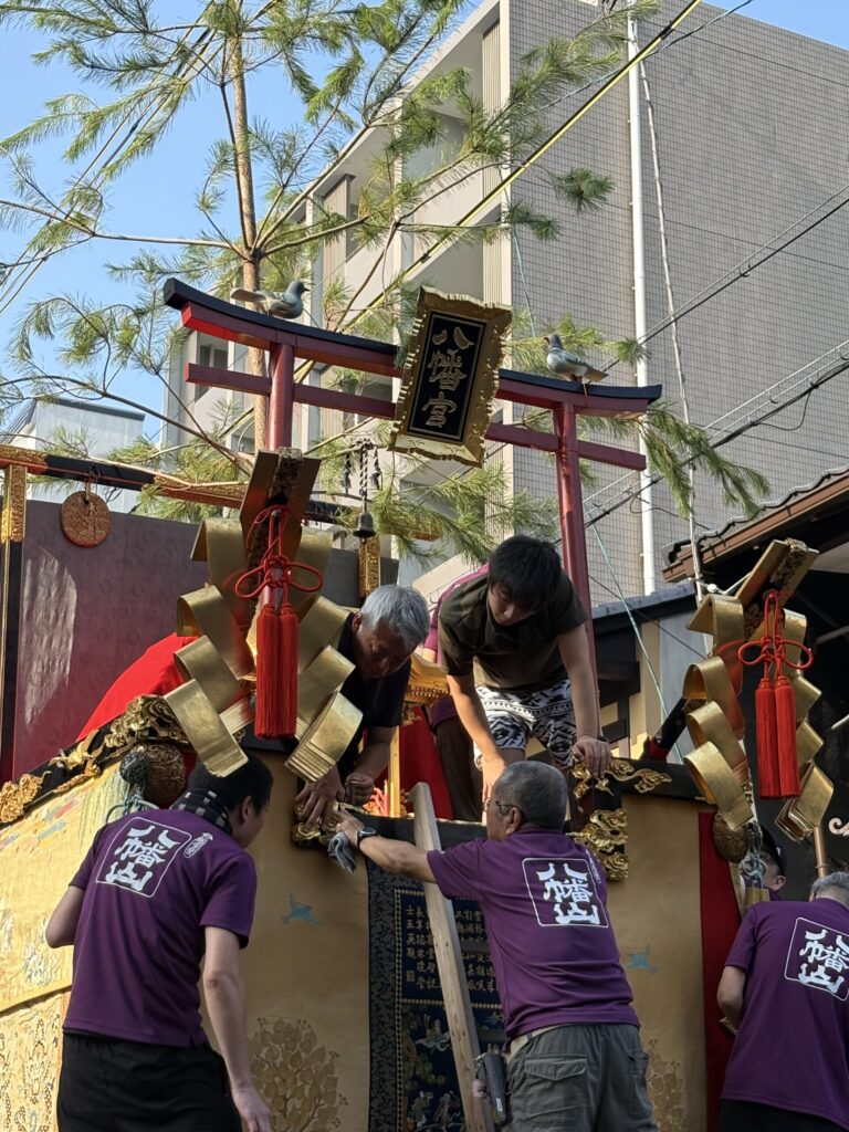祇園祭 後祭・八幡山の鳥居に据えられた二羽の鳩と、飾りを整える人たち
