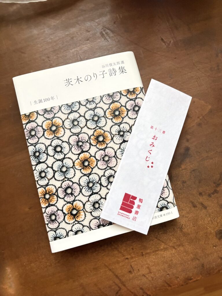 谷川俊太郎選『茨木のり子詩集』と、鴨葱書店のおみくじの短冊。表紙は小花を並べた模様