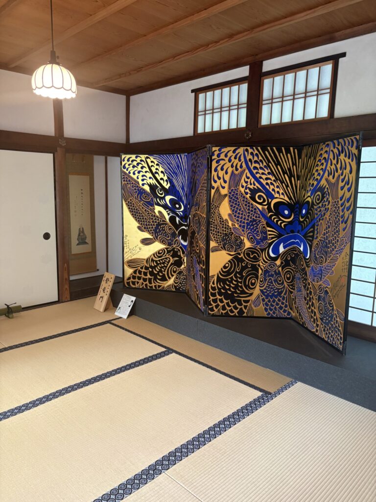 西来院の屏風「登竜門」。金地に青と黒の鯉、その奥に達磨の掛軸