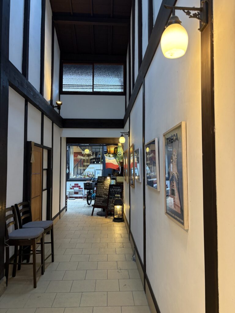 Brasserie VAPEURSへ続く路地。ポスターの並ぶ通路の先に、灯りのともる入口