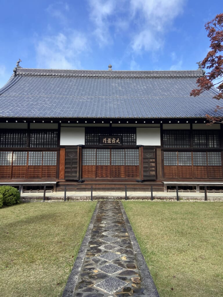 青空の下に立つ源光庵の本堂。扁額を掲げた正面へ、菱形模様の石畳がまっすぐ延びる