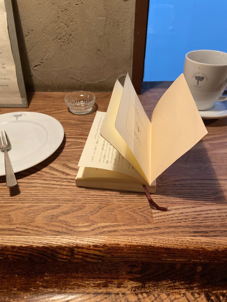 木のテーブルにひらいた本と、白い珈琲カップ